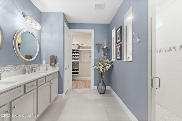 bathroom featuring double vanity, a stall shower, visible vents, tile patterned floors, and a spacious closet