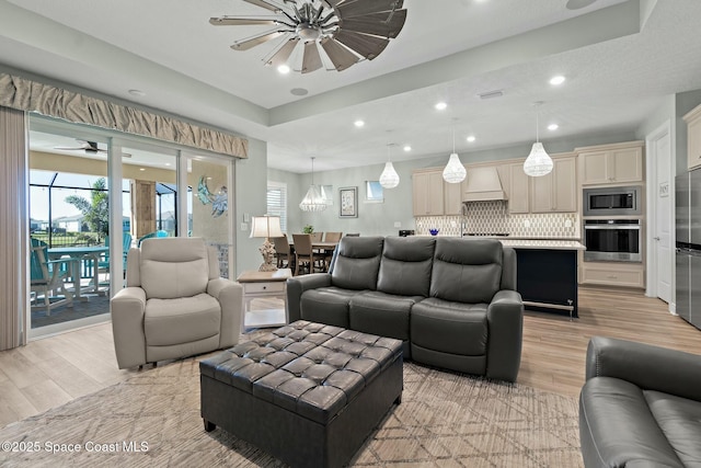 living area featuring visible vents, a raised ceiling, a ceiling fan, light wood-style flooring, and recessed lighting