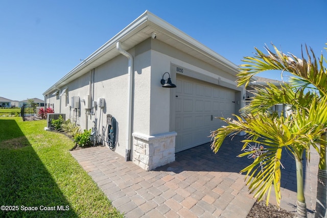 view of side of home with stone siding, a lawn, an attached garage, and stucco siding