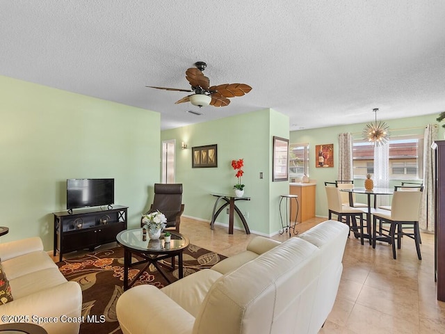 living area with ceiling fan with notable chandelier, light tile patterned floors, a textured ceiling, and baseboards