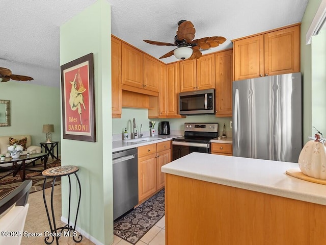 kitchen with light countertops, appliances with stainless steel finishes, a sink, a textured ceiling, and ceiling fan