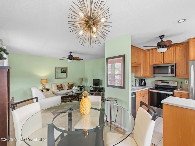 kitchen with light tile patterned floors, light countertops, appliances with stainless steel finishes, open floor plan, and ceiling fan with notable chandelier