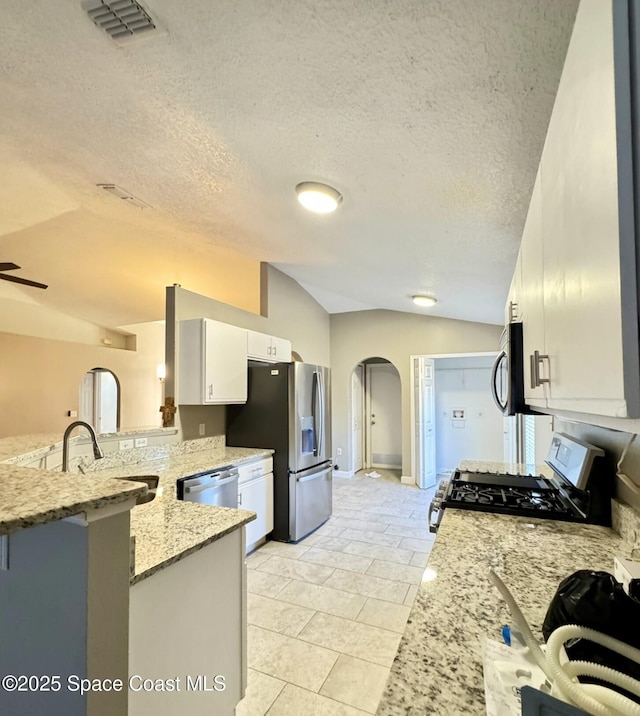 kitchen with arched walkways, light stone counters, stainless steel appliances, visible vents, and vaulted ceiling