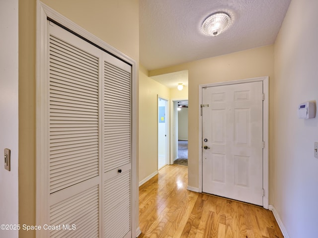 corridor featuring light wood-style flooring, a textured ceiling, and baseboards