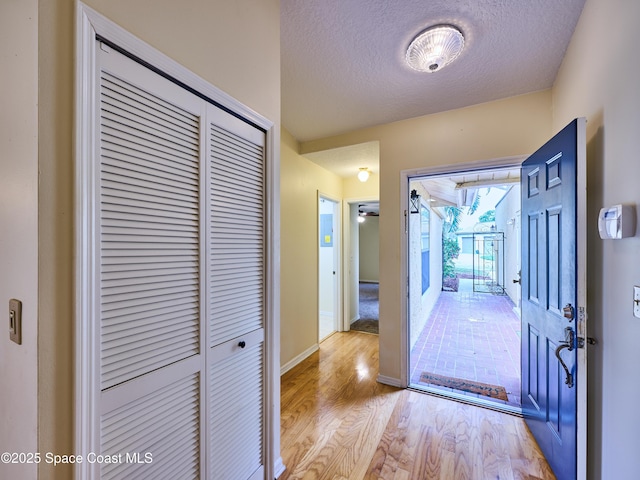 foyer featuring light wood-style floors, a textured ceiling, and baseboards