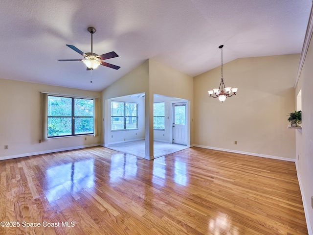 unfurnished living room featuring light wood-style flooring, vaulted ceiling, a wealth of natural light, and ceiling fan with notable chandelier