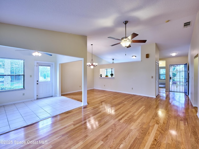 unfurnished living room featuring ceiling fan with notable chandelier, light wood-style flooring, lofted ceiling, and visible vents