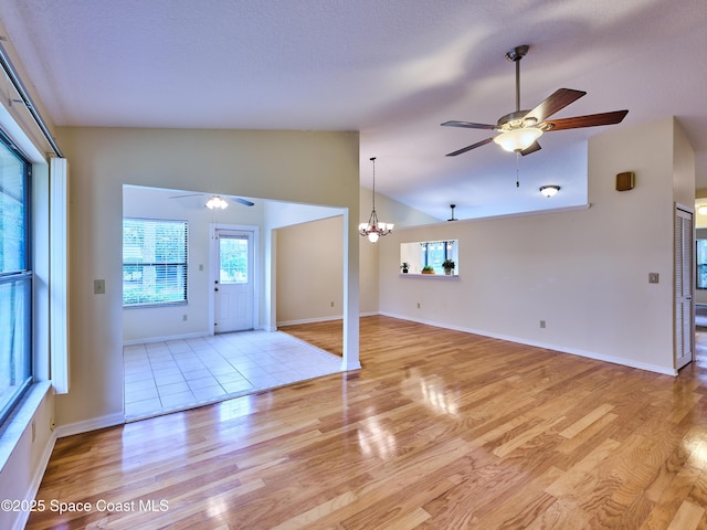 interior space featuring light wood-style floors, baseboards, vaulted ceiling, and ceiling fan with notable chandelier