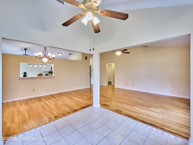 empty room with ceiling fan with notable chandelier, baseboards, vaulted ceiling, and light tile patterned flooring