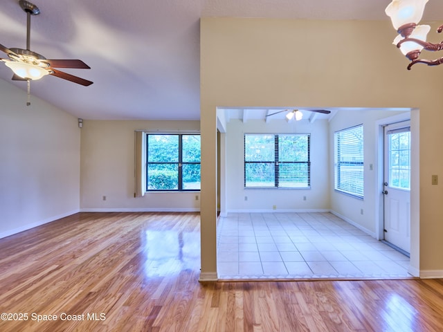 unfurnished living room featuring plenty of natural light, vaulted ceiling, and ceiling fan with notable chandelier