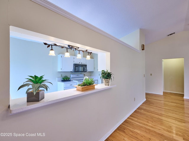 interior space with vaulted ceiling, light wood-style flooring, visible vents, and baseboards