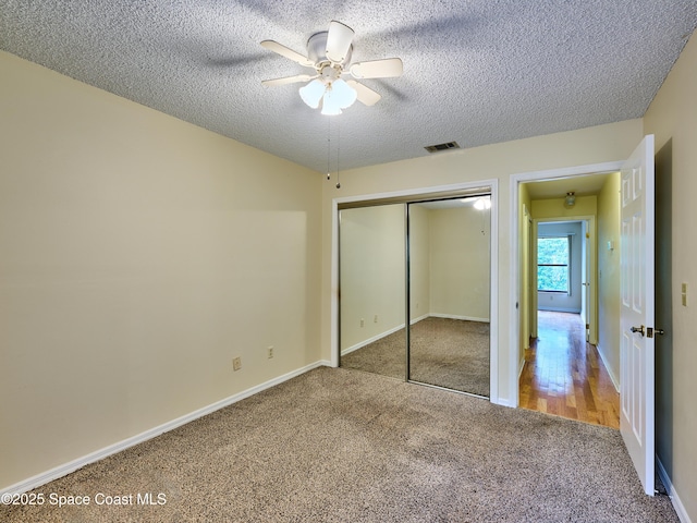 unfurnished bedroom featuring a textured ceiling, carpet floors, visible vents, a ceiling fan, and a closet