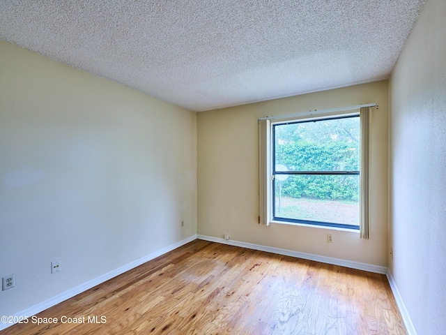 unfurnished room with a textured ceiling, light wood-type flooring, and baseboards