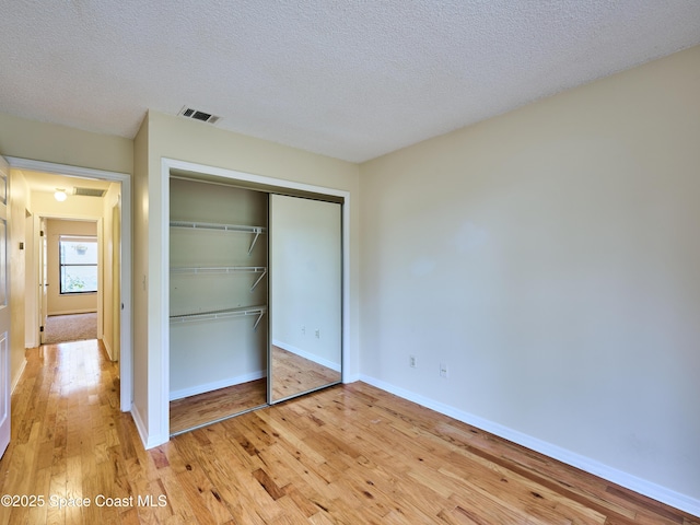 unfurnished bedroom with light wood-style flooring, a textured ceiling, visible vents, and a closet