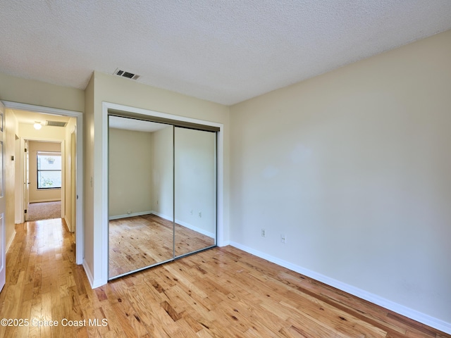 unfurnished bedroom with baseboards, visible vents, light wood-style flooring, a textured ceiling, and a closet