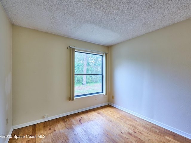 spare room with a textured ceiling, baseboards, and wood finished floors