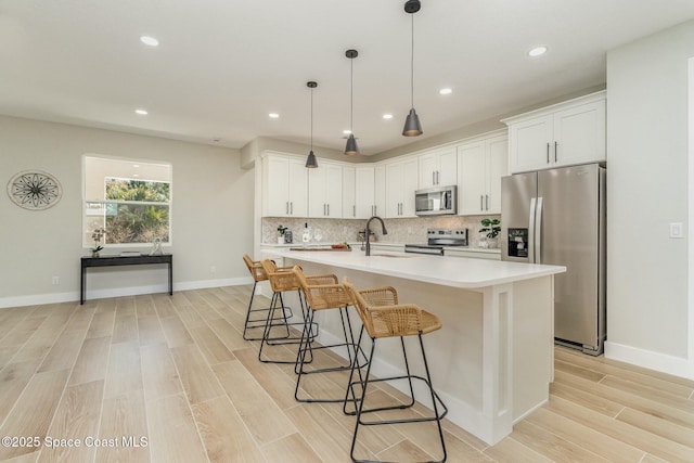 kitchen with stainless steel appliances, tasteful backsplash, light countertops, light wood-style floors, and a sink