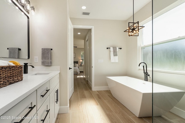 ensuite bathroom with visible vents, connected bathroom, vanity, a freestanding tub, and wood finish floors