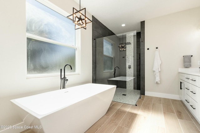 bathroom with wood finish floors, vanity, a freestanding tub, baseboards, and walk in shower