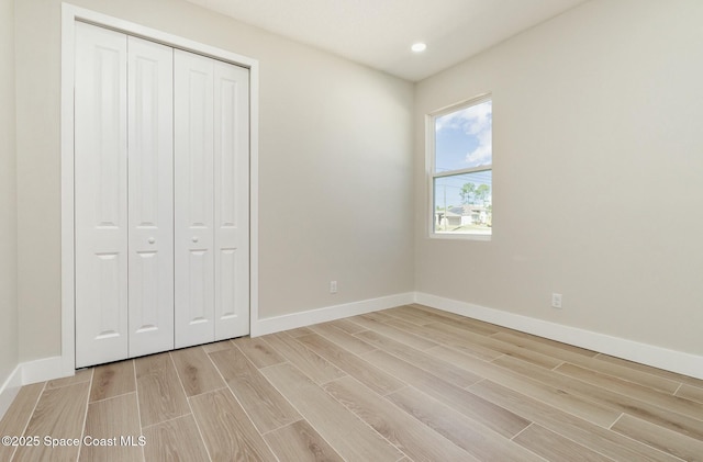 unfurnished bedroom with wood finish floors, a closet, baseboards, and recessed lighting