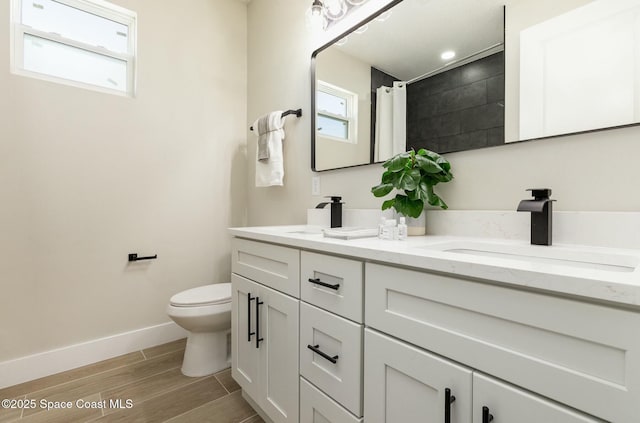 bathroom with double vanity, toilet, a sink, wood finished floors, and baseboards