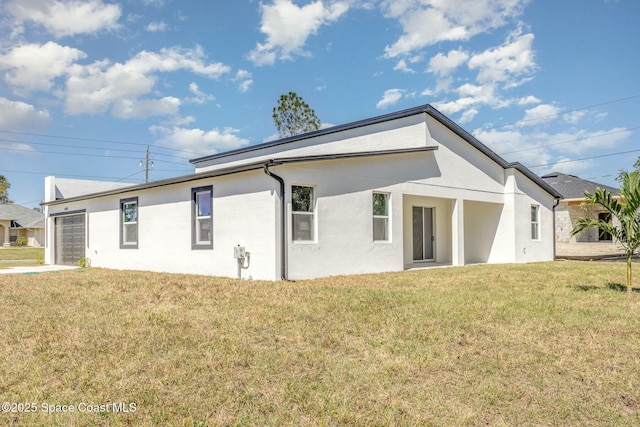 rear view of property featuring driveway, a lawn, an attached garage, and stucco siding