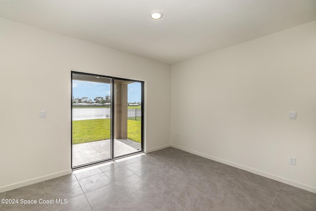 empty room featuring a water view, tile patterned flooring, and baseboards