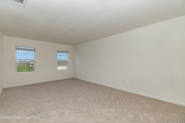 unfurnished room featuring light colored carpet, visible vents, a textured ceiling, and baseboards