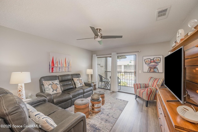 living area with a ceiling fan, a textured ceiling, visible vents, and wood finished floors