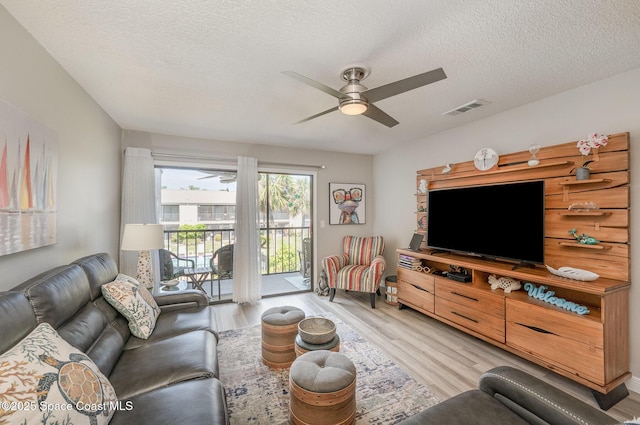 living room with a ceiling fan, visible vents, light wood-style flooring, and a textured ceiling