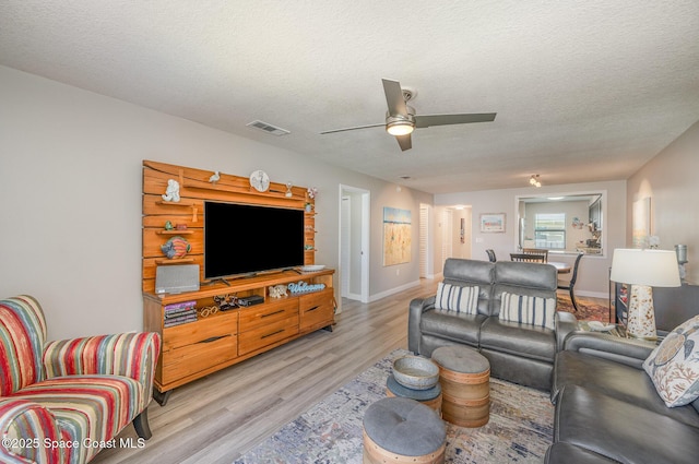 living area featuring light wood-style floors, visible vents, a textured ceiling, and a ceiling fan