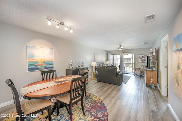 dining room with baseboards, light wood-style flooring, visible vents, and a textured ceiling