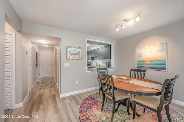 dining area featuring light wood-type flooring, a textured ceiling, and baseboards