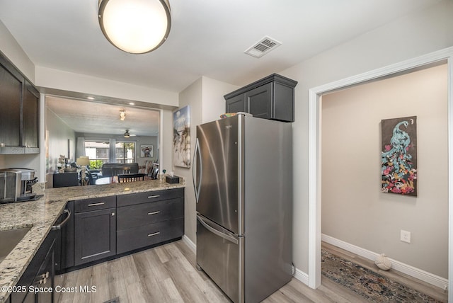 kitchen with visible vents, light wood finished floors, freestanding refrigerator, and light stone countertops