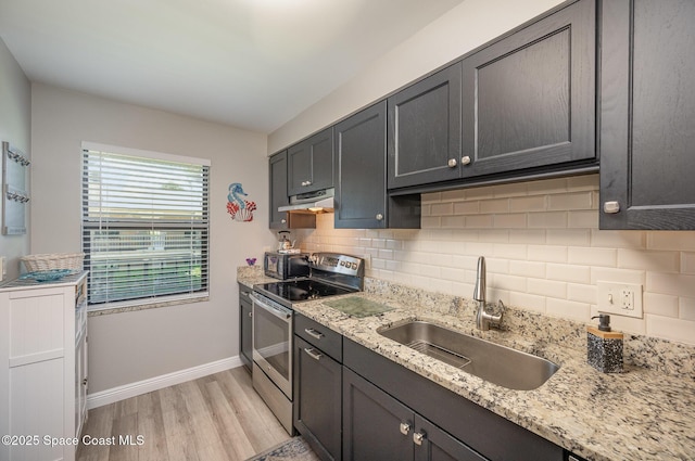 kitchen with under cabinet range hood, a sink, decorative backsplash, light wood finished floors, and stainless steel range with electric stovetop