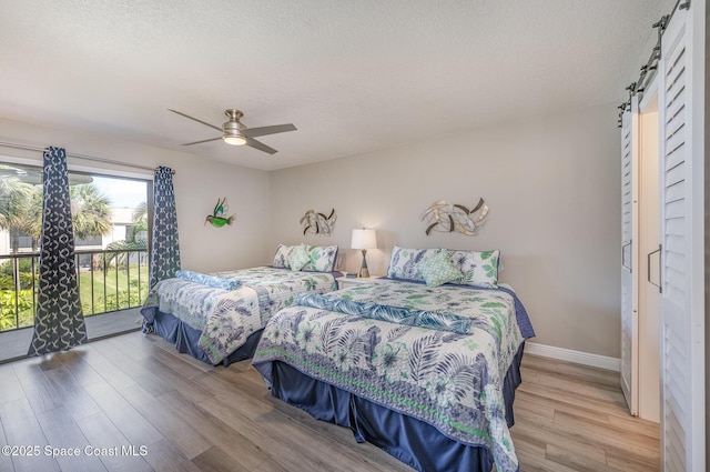 bedroom featuring a barn door, baseboards, wood finished floors, access to exterior, and a textured ceiling