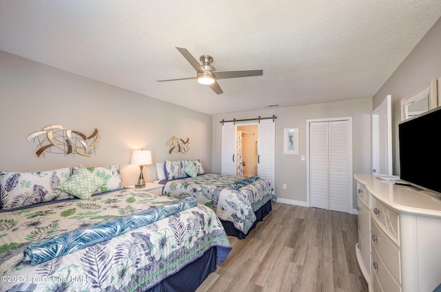 bedroom featuring a textured ceiling, a barn door, light wood-style flooring, visible vents, and a closet