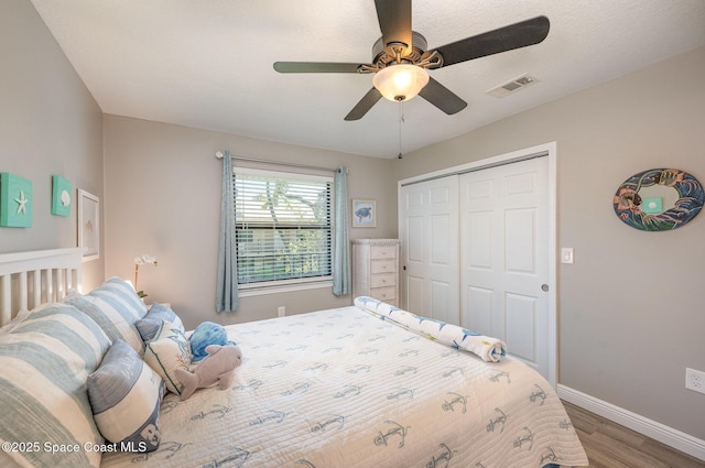 bedroom with baseboards, visible vents, a ceiling fan, wood finished floors, and a closet