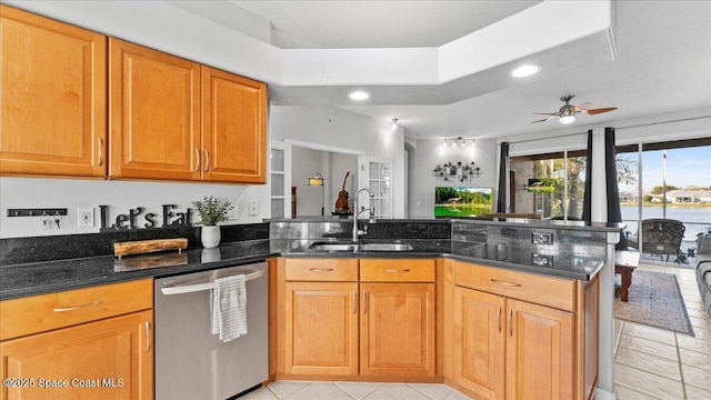 kitchen featuring a peninsula, a sink, dishwasher, brown cabinetry, and dark stone countertops