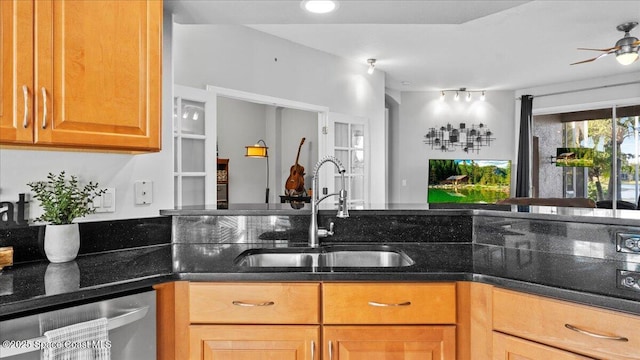 kitchen with stainless steel dishwasher, ceiling fan, dark stone counters, and a sink