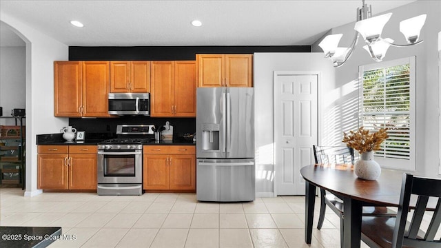 kitchen with arched walkways, a notable chandelier, dark countertops, appliances with stainless steel finishes, and brown cabinetry