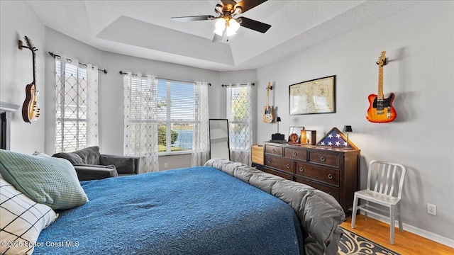 bedroom featuring baseboards, a textured ceiling, a tray ceiling, and wood finished floors