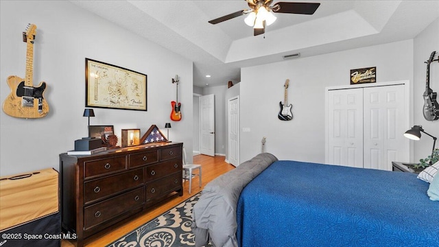 bedroom with multiple closets, a tray ceiling, visible vents, and light wood finished floors