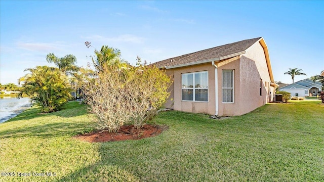 view of side of home featuring a water view, central AC, a lawn, and stucco siding