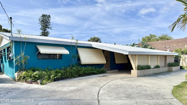 view of front of house featuring a carport, concrete driveway, metal roof, and stucco siding