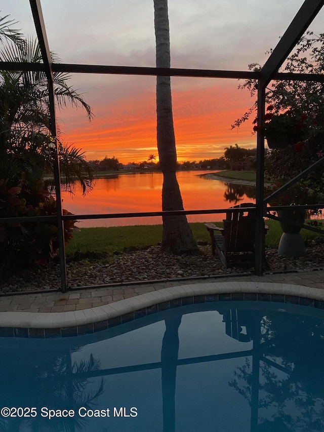 pool at dusk featuring a lanai, a patio area, an outdoor pool, and a water view