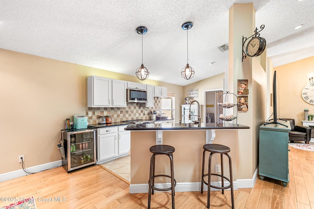 kitchen featuring a kitchen bar, beverage cooler, stainless steel microwave, dark countertops, and lofted ceiling