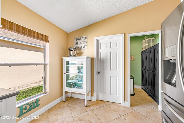 doorway to outside featuring baseboards, a textured ceiling, light tile patterned flooring, and vaulted ceiling