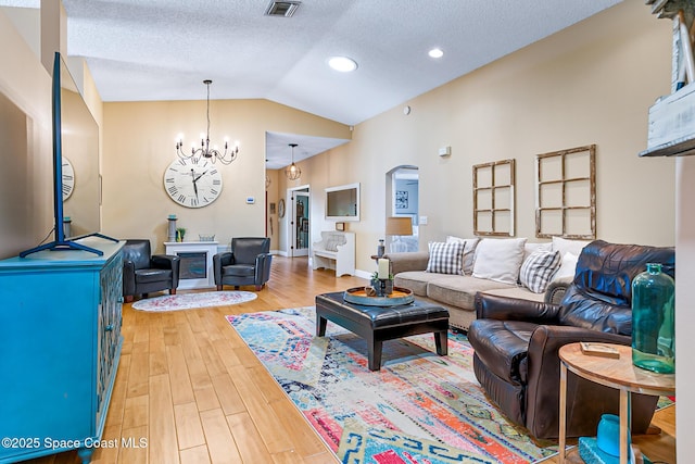 living area featuring visible vents, lofted ceiling, arched walkways, a notable chandelier, and light wood-type flooring