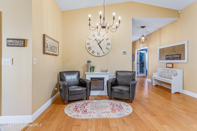 living area with baseboards, an inviting chandelier, wood finished floors, and vaulted ceiling